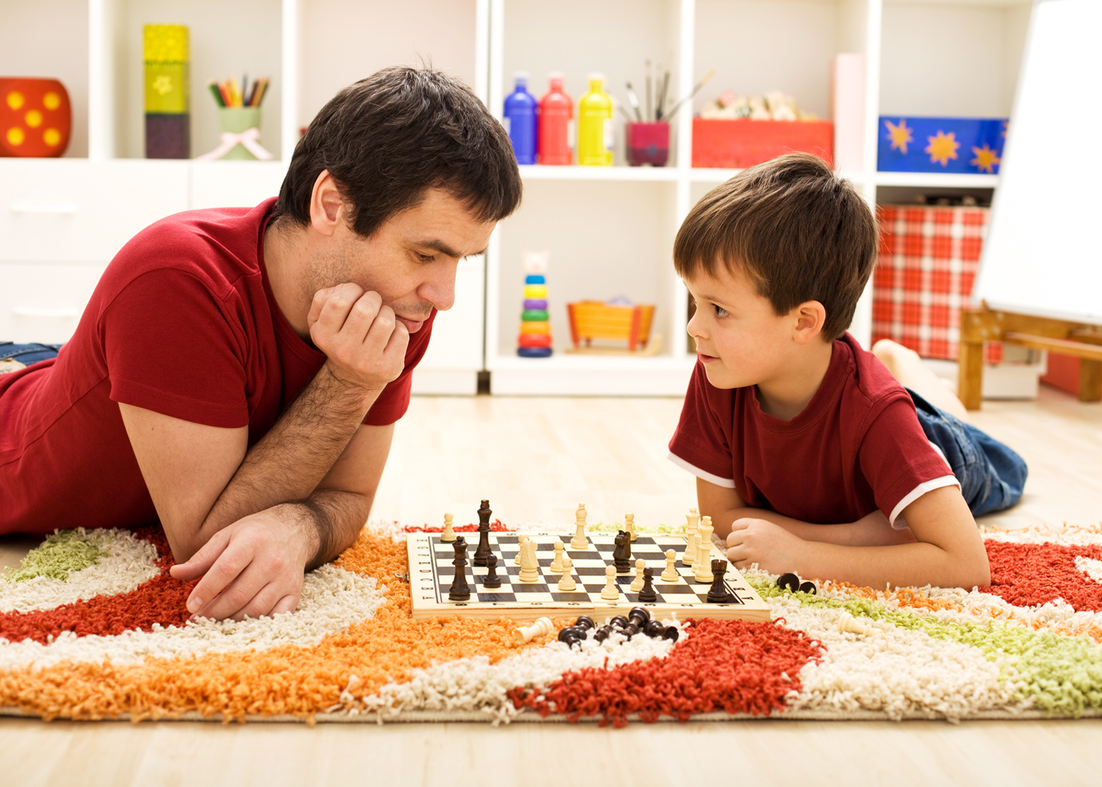 Man teaching boy the rules of chess - playing on the floor in the kids room